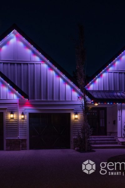 A modern farmhouse-style home adorned with vibrant, multicolored LED lighting along its gable roofs and eaves, creating a festive ambiance at night.