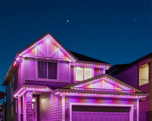 A two-story house with a garage, adorned with vibrant purple and pink LED lights along its roof edges and gutters, set against a dark night sky filled with stars.